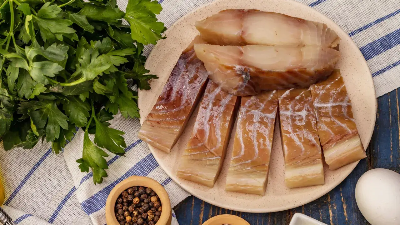 Wędzony czarniak, podobny do dorsza, pokrojony na kawałki, leży na talerzu obok świeżej natki pietruszki i pieprzu.