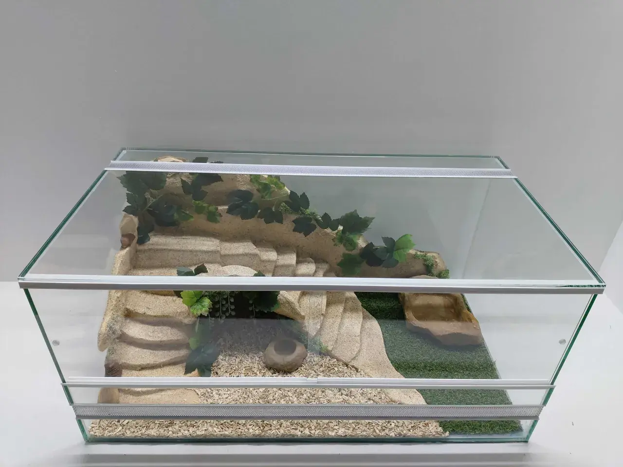 Piękne terrarium dla żółwia greckiego z piaskowcem, sztuczną trawą i kryjówkami. Idealne miejsce do eksploracji i odpoczynku.